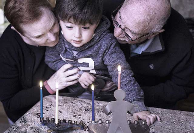 Grandparents gather around the menorah with their grandson.